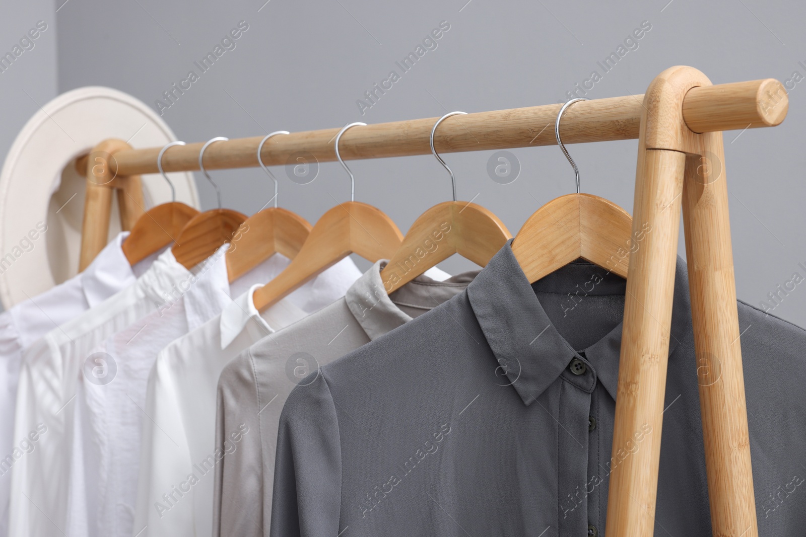Photo of Rack with different stylish shirts on wooden hangers against grey wall, closeup. Organizing clothes