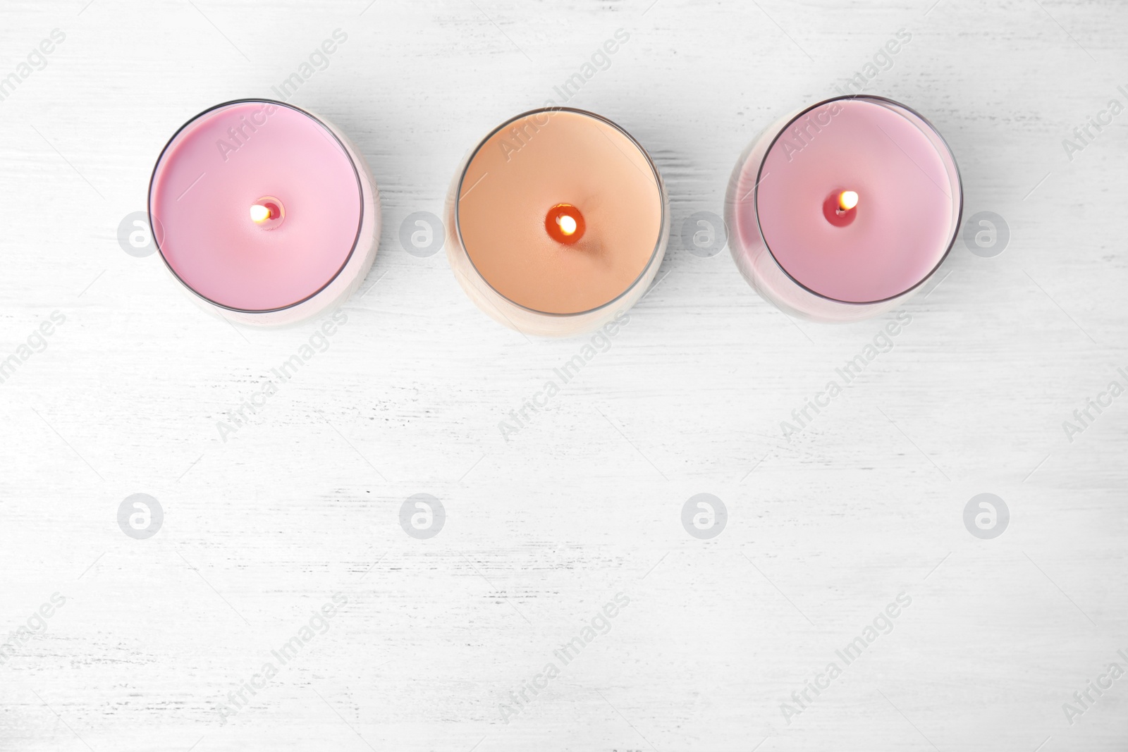 Photo of Color wax candles in glass holders on white wooden table, flat lay. Space for text