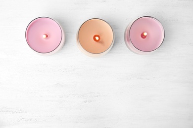 Photo of Color wax candles in glass holders on white wooden table, flat lay. Space for text