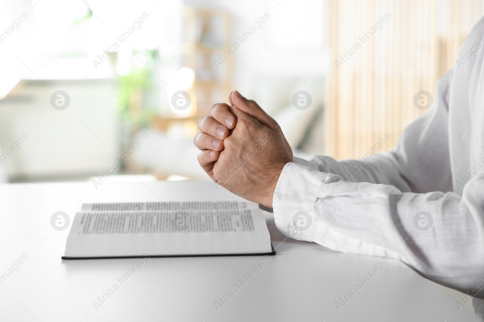 Photo of Man with Bible praying at white table indoors, closeup