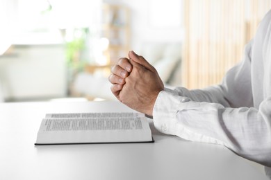 Man with Bible praying at white table indoors, closeup