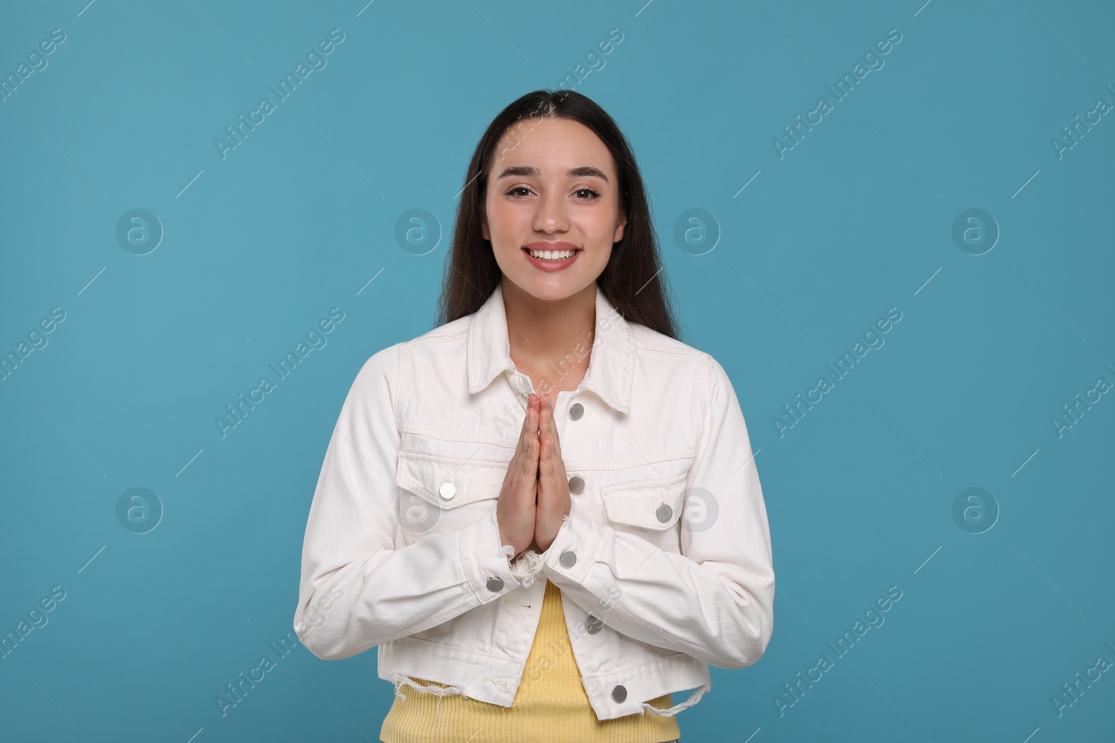 Photo of Thank you gesture. Beautiful grateful woman with hands clasped together on light blue background