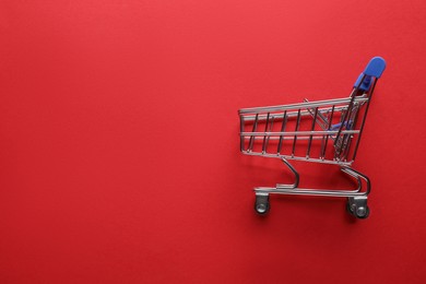 Small metal shopping cart on red background, top view. Space for text