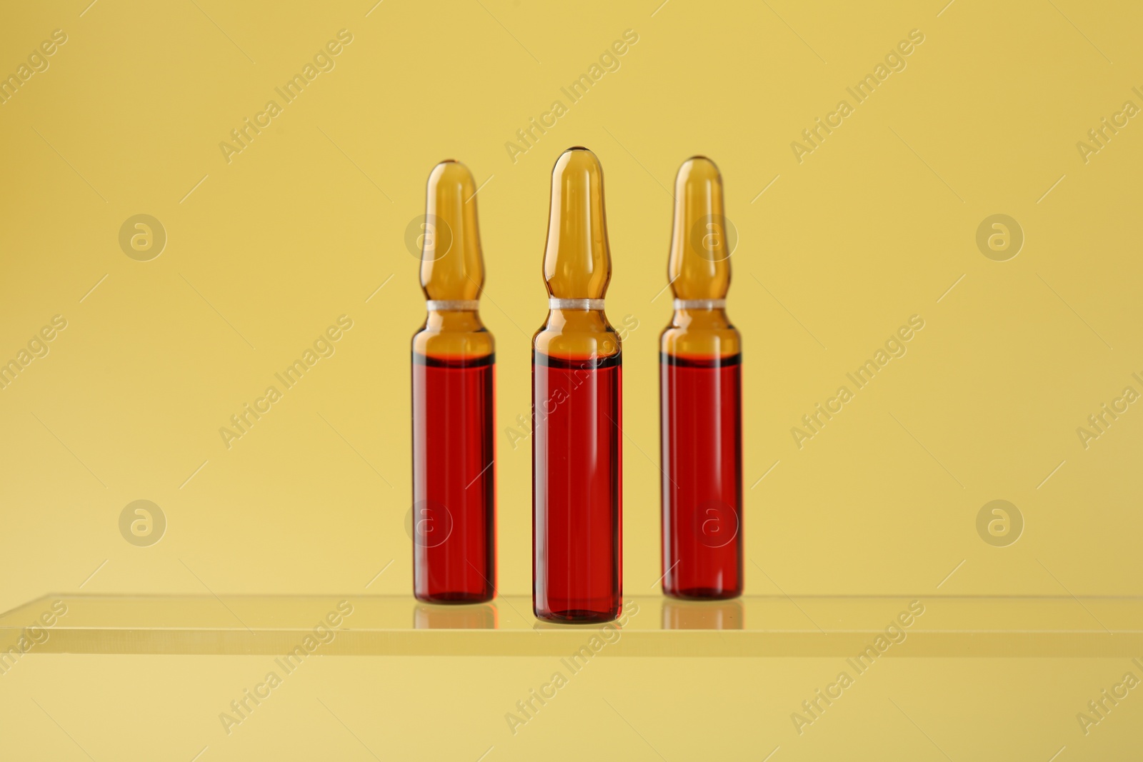 Photo of Glass ampoules with liquid on yellow background