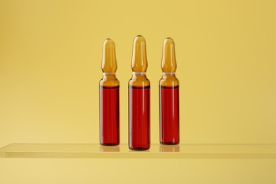 Photo of Glass ampoules with liquid on yellow background