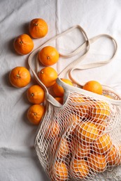 Photo of Net bag with many fresh ripe tangerines on white cloth, flat lay