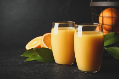 Photo of Glasses of orange juice and fresh fruits on black table. Space for text