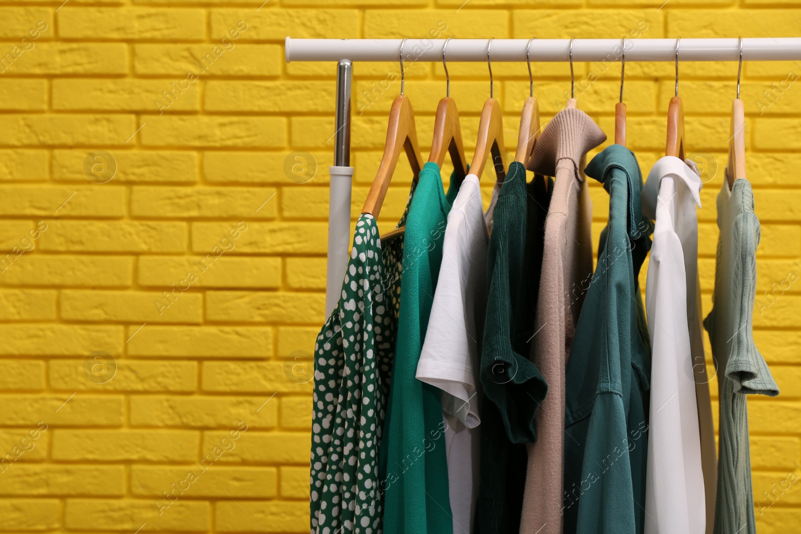 Photo of Rack with different stylish clothes near yellow brick wall. Space for text