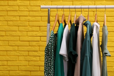 Rack with different stylish clothes near yellow brick wall. Space for text