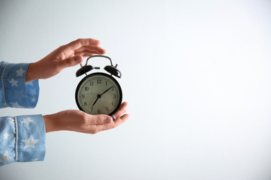 Woman holding alarm clock on white background, closeup. Morning time