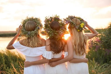 Photo of Young women wearing wreaths made of flowers outdoors at sunset, back view