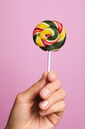 Woman holding bright tasty lollipop on pink background, closeup