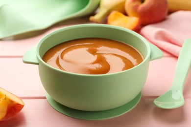 Bowl with tasty pureed baby food and ingredients on pink wooden table, closeup