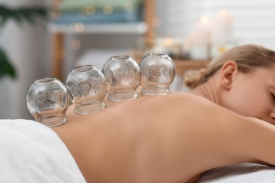 Cupping therapy. Woman with glass cup on massage couch in spa salon, closeup
