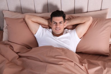 Photo of Man lying in comfortable bed with beige linens, above view