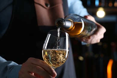 Photo of Bartender pouring white wine from bottle into glass indoors, closeup