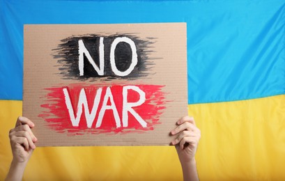 Photo of Teenage boy holding poster No War against Ukrainian flag, closeup. Space for text