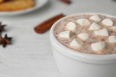 Delicious hot cocoa drink with marshmallows in cup on white wooden table, closeup