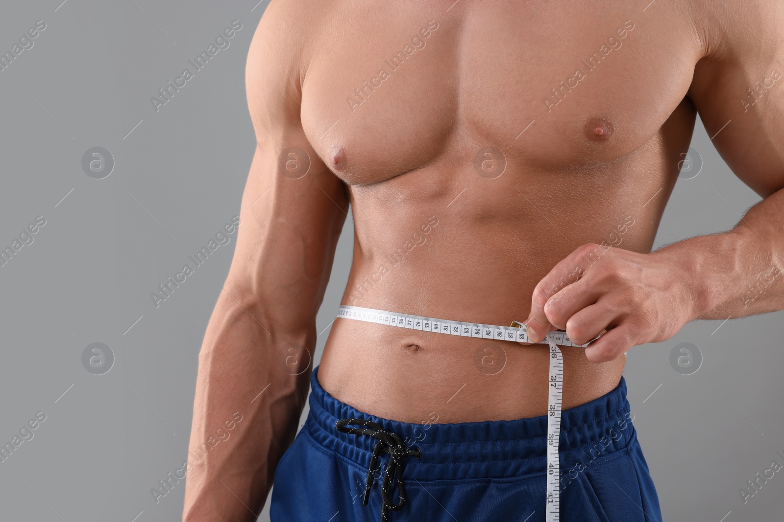 Photo of Athletic man measuring waist with tape on grey background, closeup. Weight loss concept