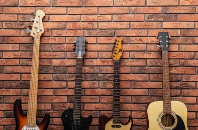 Photo of Modern electric and classical guitars near red brick wall