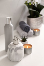 Photo of Soap dispenser and burning candle on countertop in bathroom. Space for text