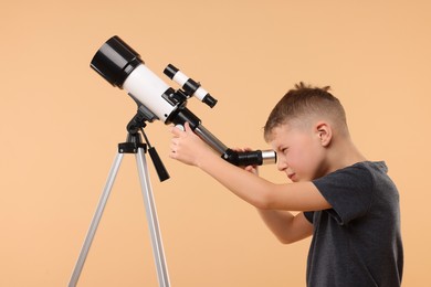 Little boy looking at stars through telescope on beige background