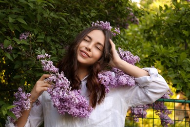 Attractive young woman near blooming lilac bush outdoors