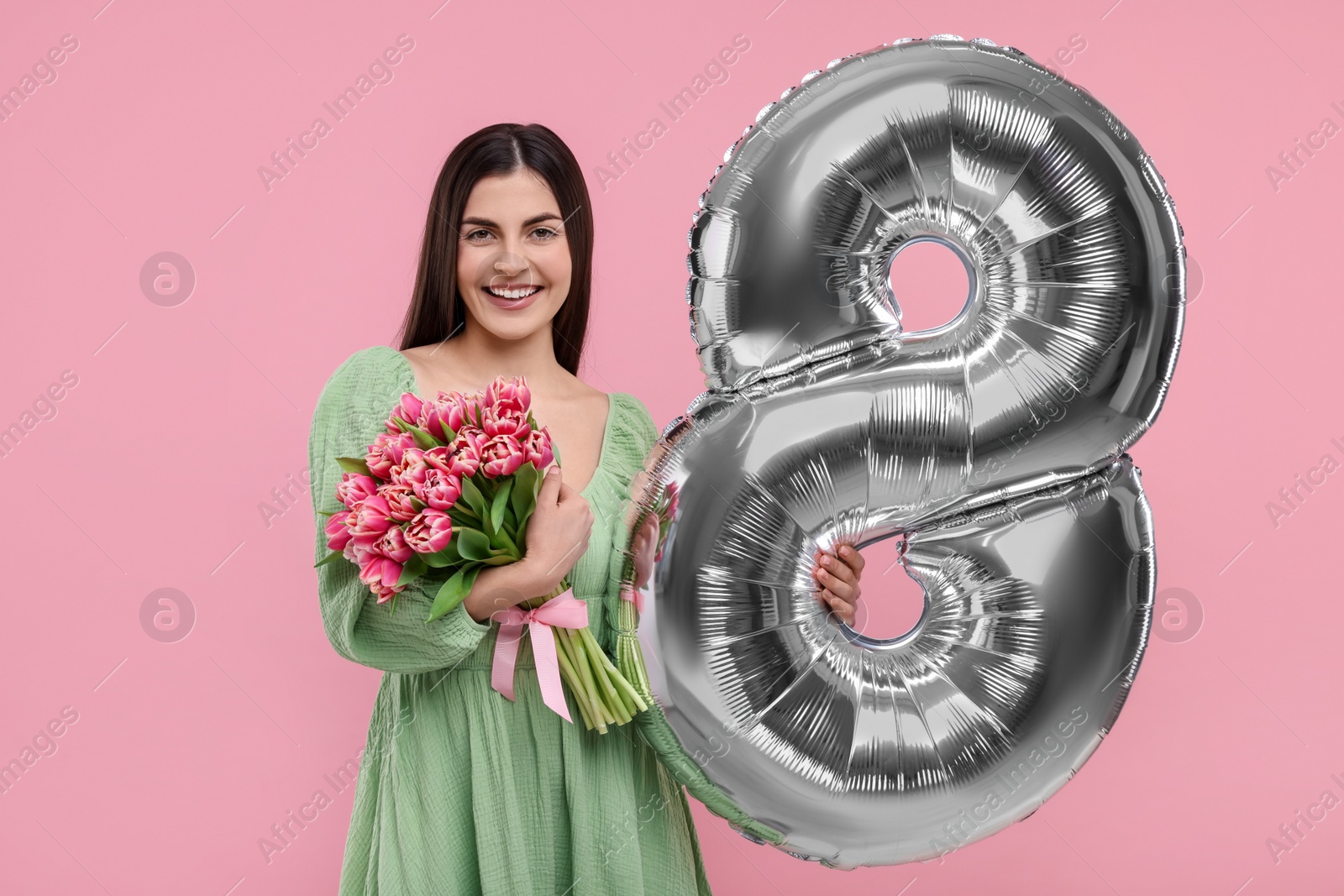 Photo of Happy Women's Day. Charming lady holding bouquet of beautiful flowers and balloon in shape of number 8 on pink background