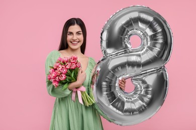 Photo of Happy Women's Day. Charming lady holding bouquet of beautiful flowers and balloon in shape of number 8 on pink background