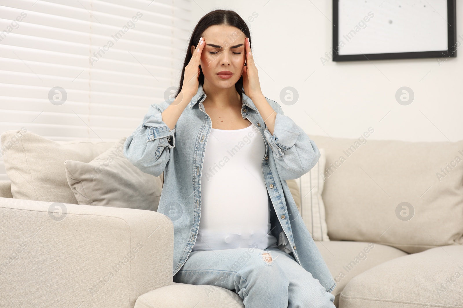 Photo of Pregnant woman suffering from headache on sofa at home