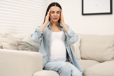 Pregnant woman suffering from headache on sofa at home