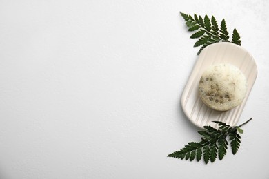 Top view of soap bar with dish and green leaves on white background, space for text. Eco friendly personal care product