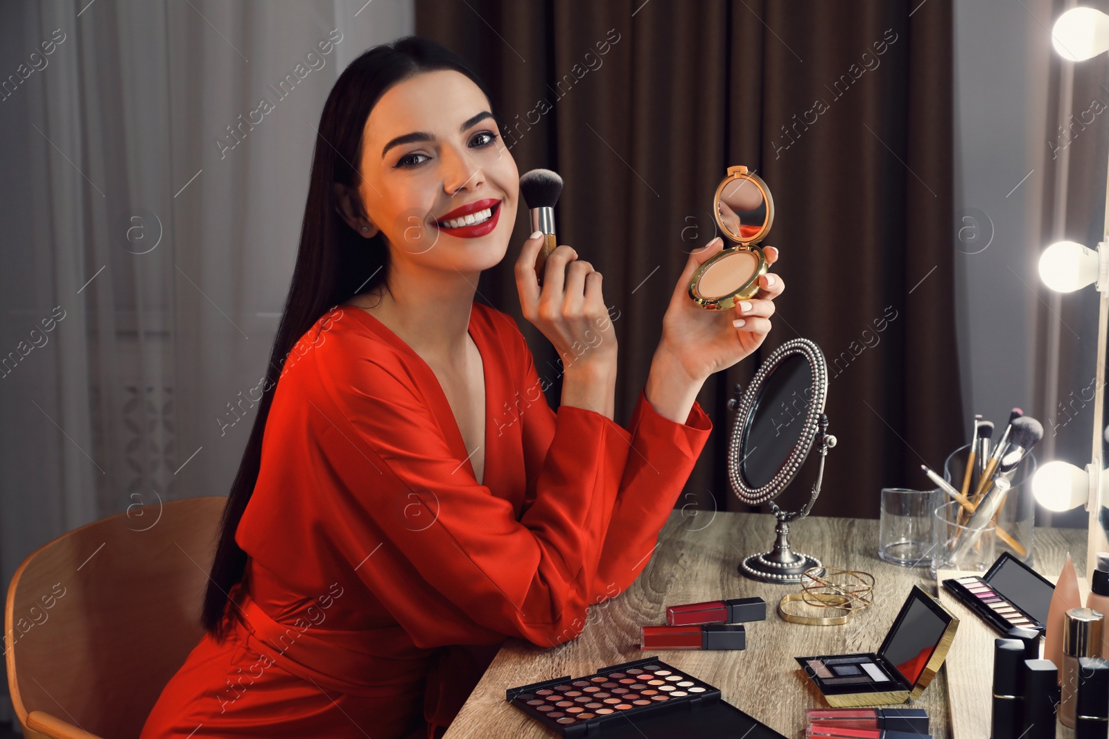 Photo of Beautiful woman applying makeup near mirror in room