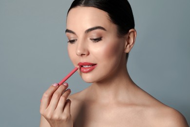 Photo of Pretty young woman applying beautiful pink lip pencil on grey background