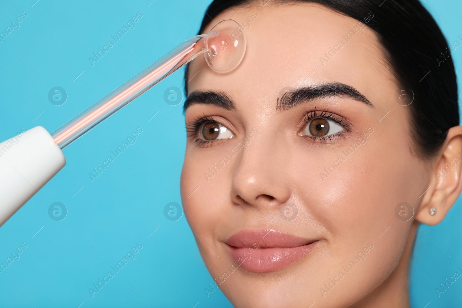 Photo of Woman using high frequency darsonval device on light blue background, closeup