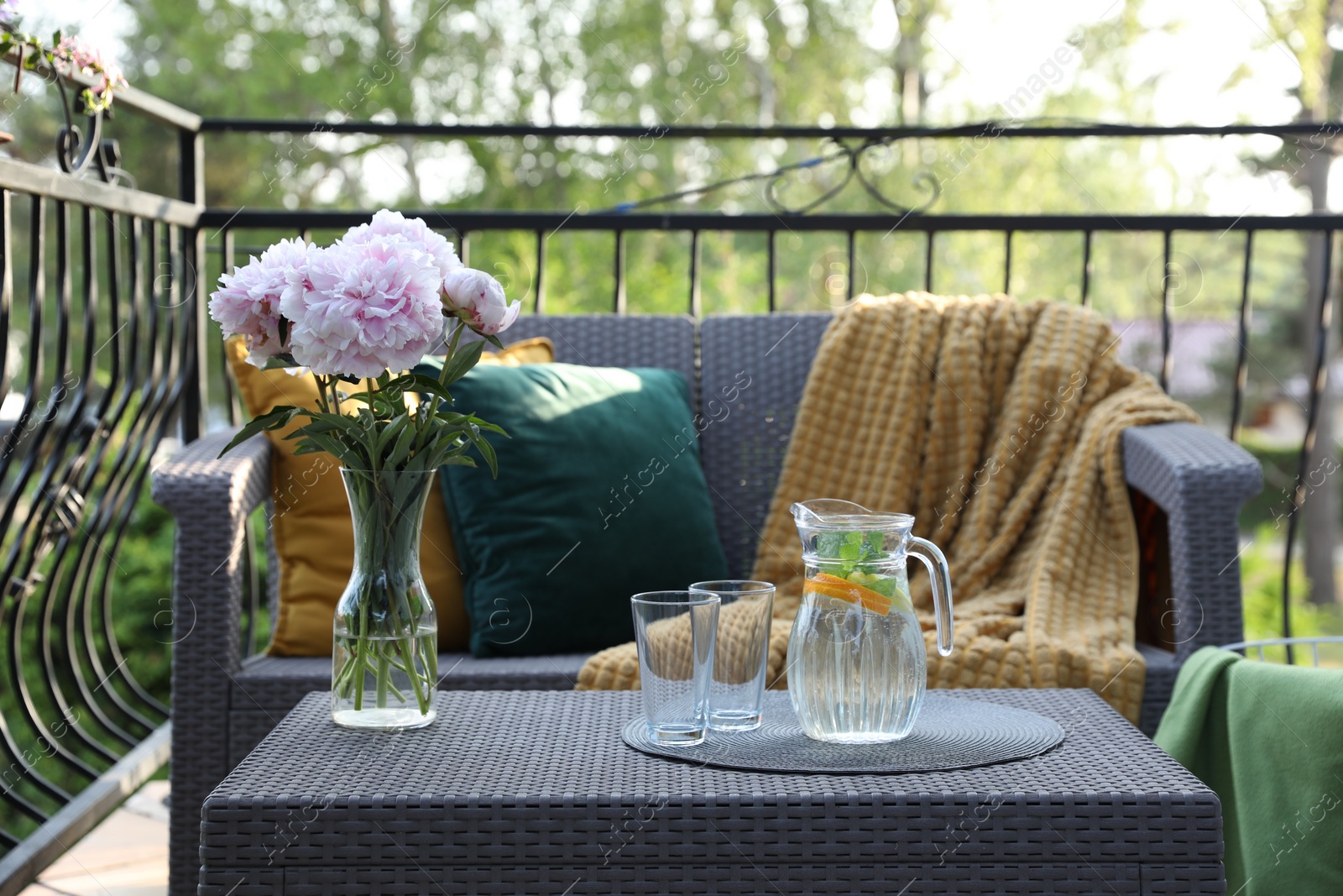 Photo of Rattan table with jug of water, glasses and beautiful flowers on terrace