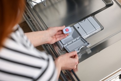 Photo of Woman putting detergent tablet into open dishwasher, closeup