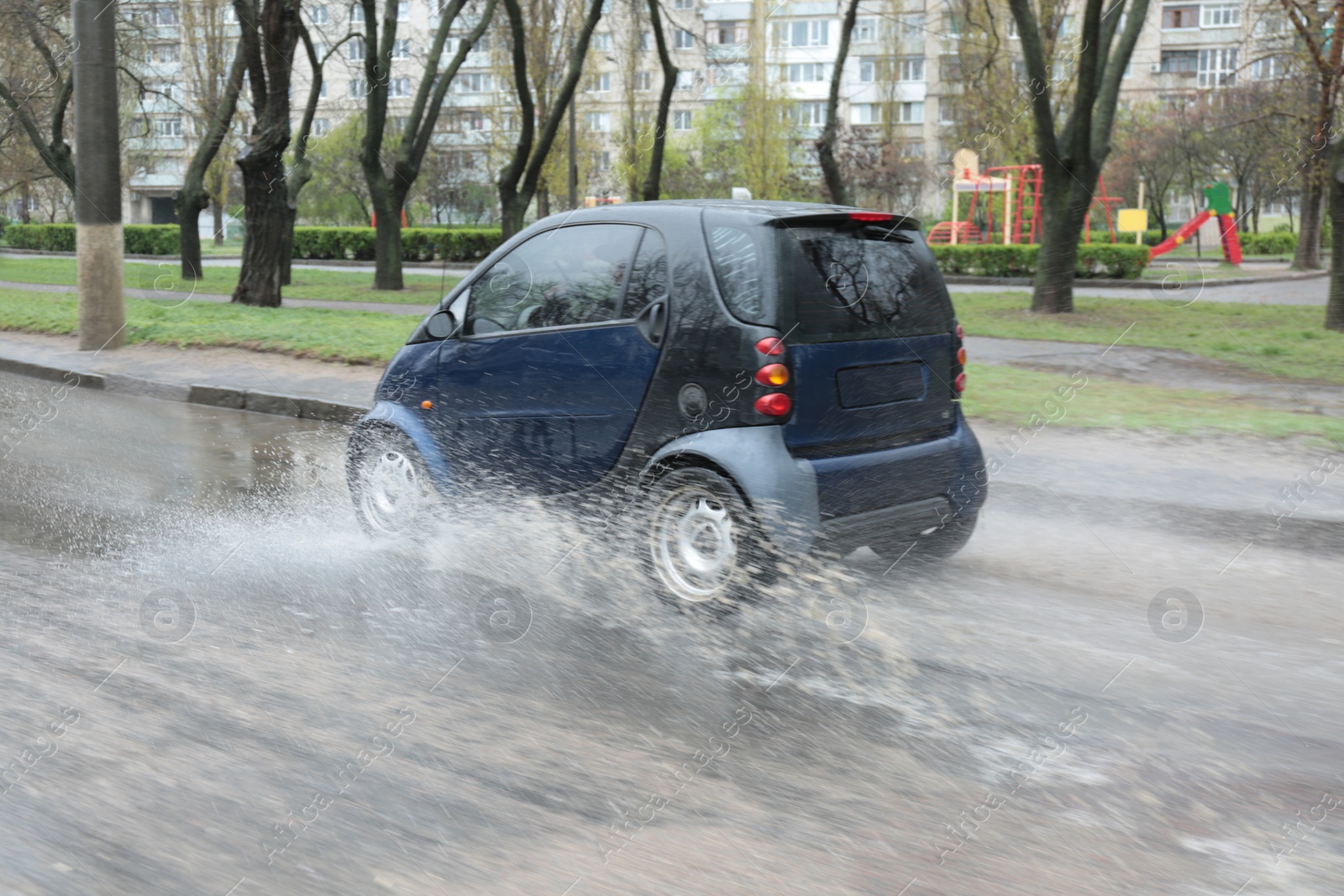 Photo of Car driving through large puddle outdoors on rainy day