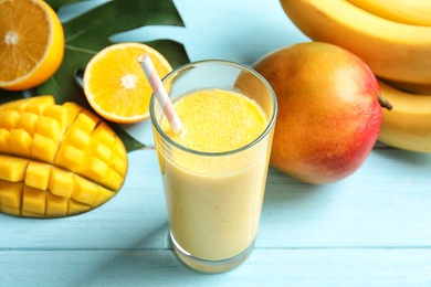 Glass of fresh mango drink and tropical fruits on color wooden table