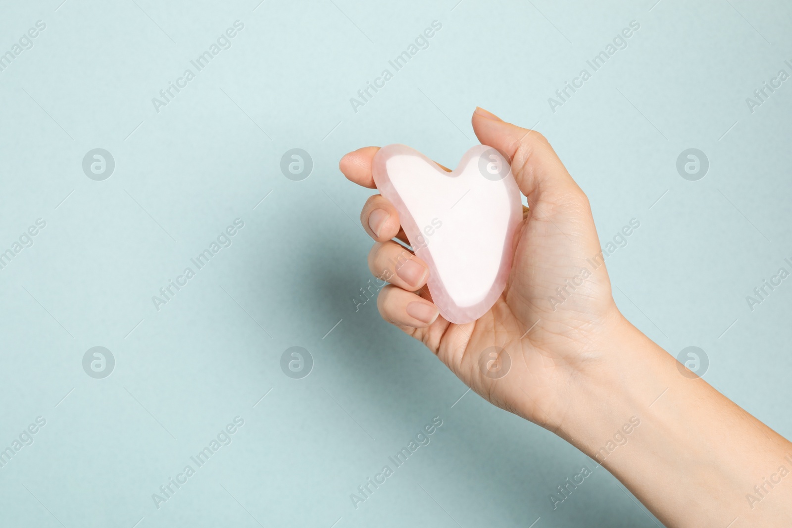 Photo of Woman with rose quartz gua sha tool on light background, closeup. Space for text