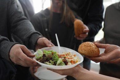 Poor man receiving food from volunteer indoors, closeup