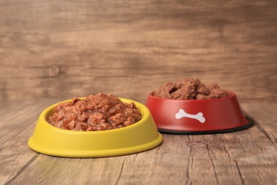 Photo of Wet pet food in feeding bowls on wooden floor