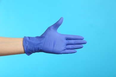 Photo of Person in medical gloves on light blue background, closeup of hand