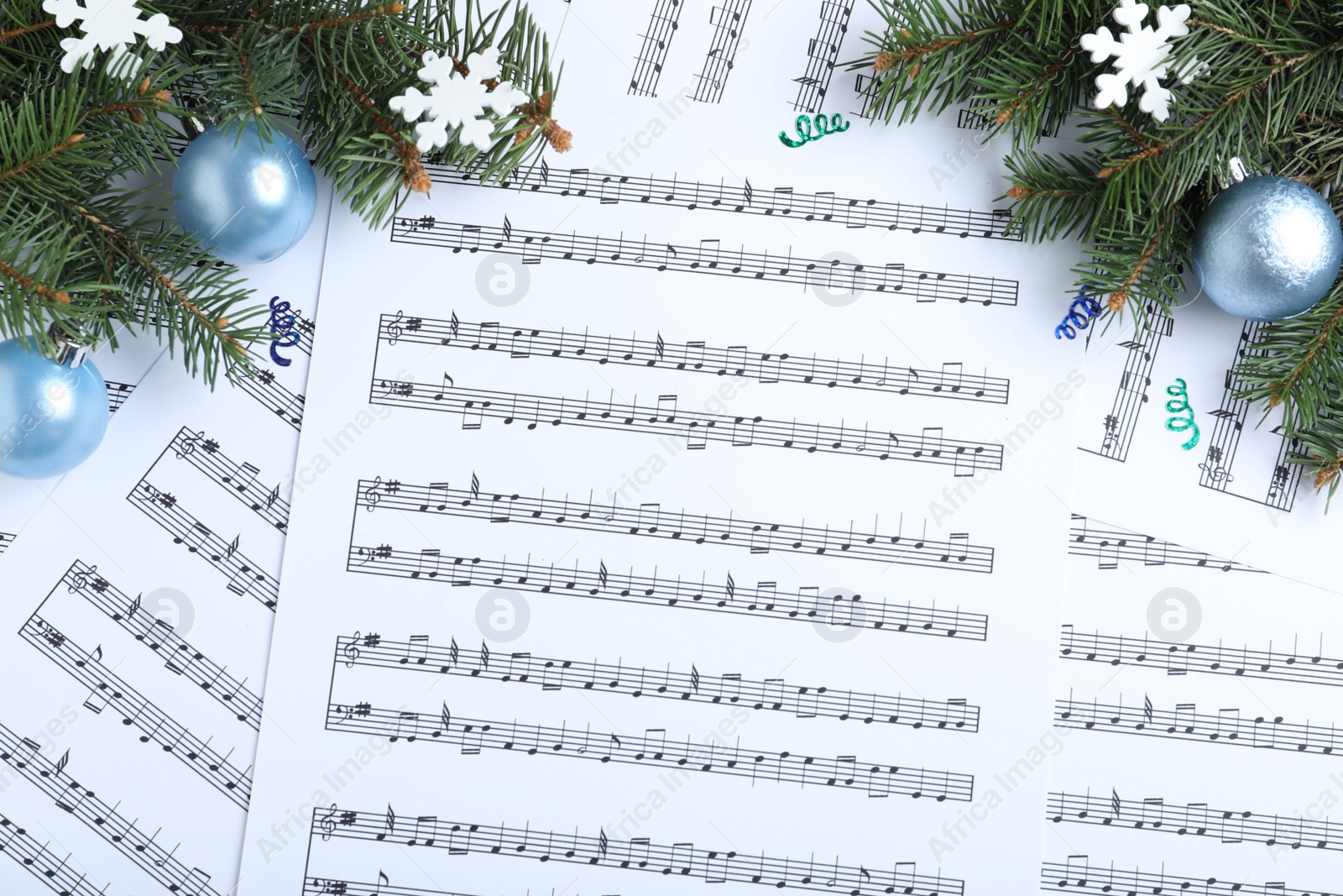 Photo of Fir branches, decorative snowflakes and light blue balls on Christmas music sheets, flat lay