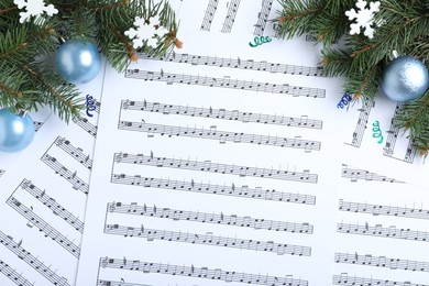 Photo of Fir branches, decorative snowflakes and light blue balls on Christmas music sheets, flat lay