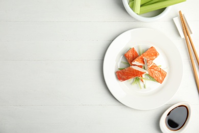 Photo of Fresh crab sticks with cucumber and soy sauce served on white wooden table, flat lay. Space for text