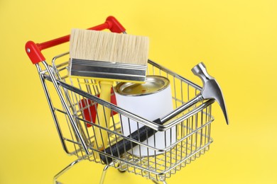 Photo of Small shopping cart with paint and renovation equipment on yellow background