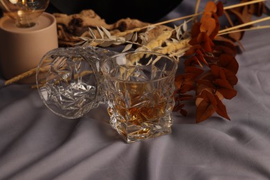 Photo of Glass of tasty alcoholic drink, empty one and decorative plants on grey fabric, closeup