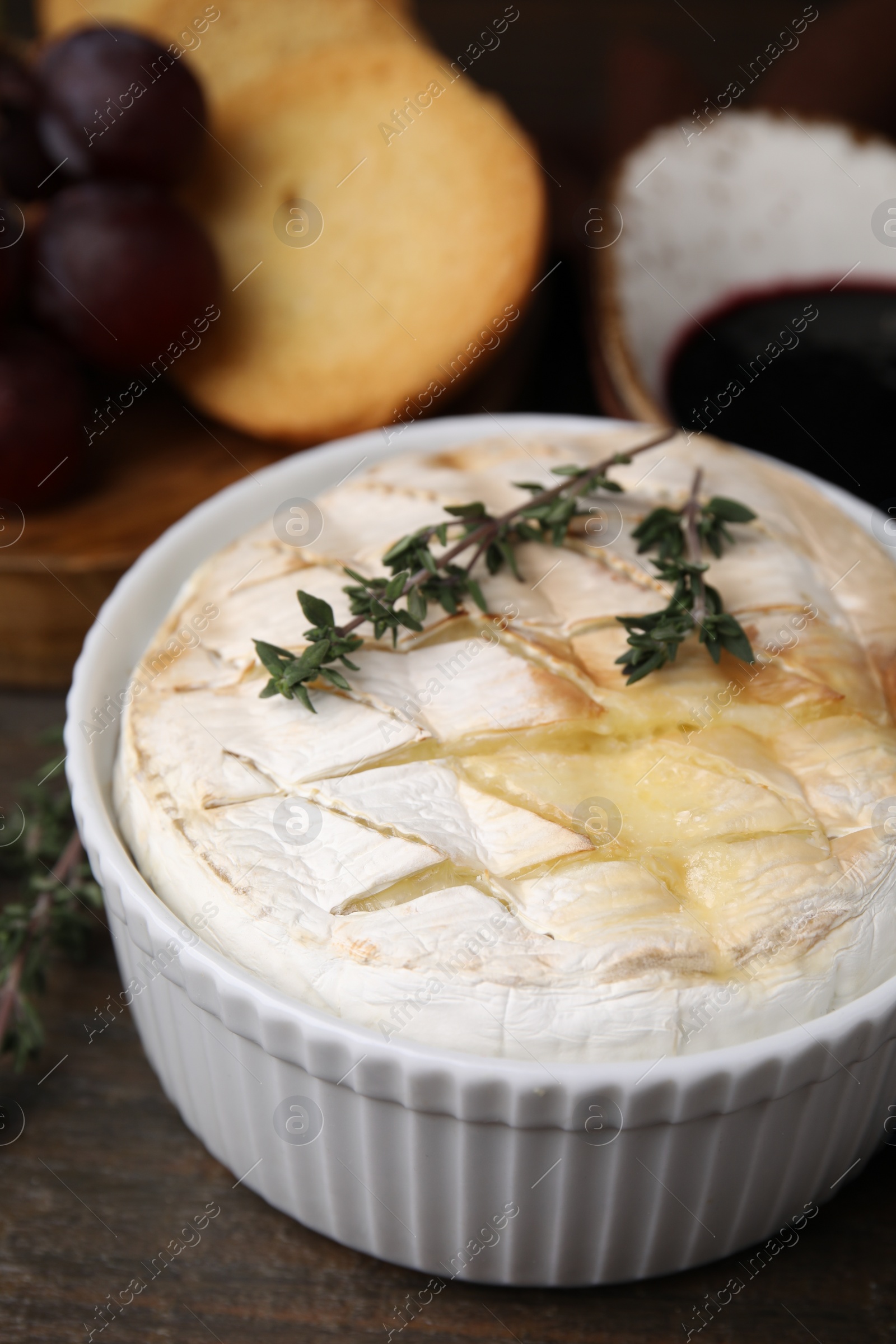 Photo of Tasty baked camembert and thyme in bowl on wooden table, closeup