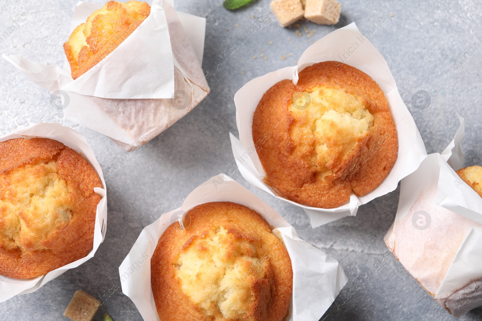 Photo of Delicious sweet muffins and brown sugar on light grey textured table, flat lay